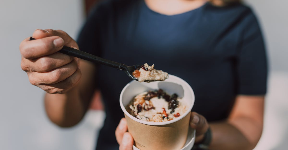 Close-up of a person holding a bowl of vegan oatmeal topped with fruits.