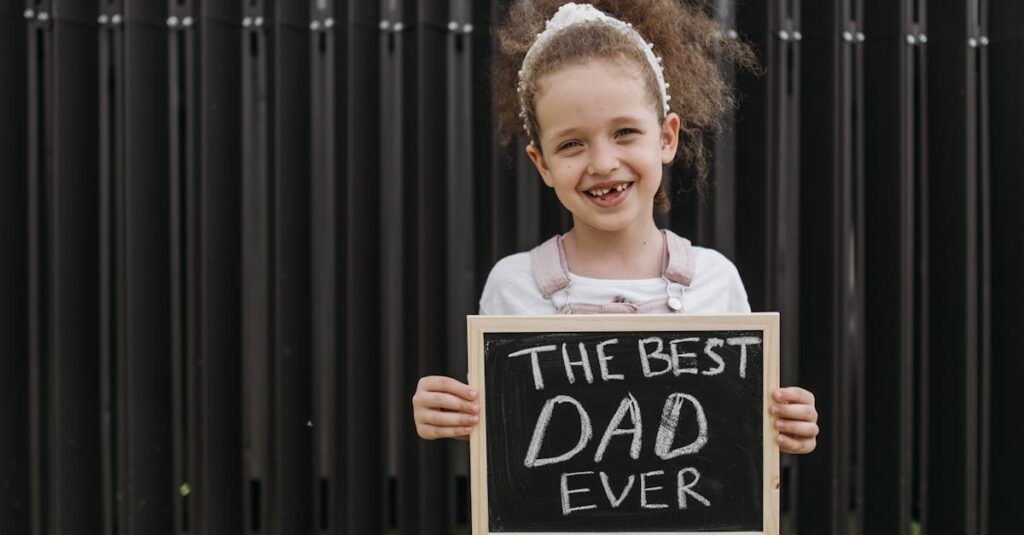 Cheerful young girl holding a blackboard with 'The Best Dad Ever' sign in a playful outdoor setting. Father's Day Gifts