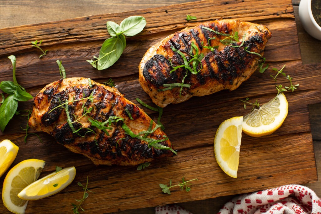 Grilled chicken breast with fresh lemon and herbs on a rustic wooden board