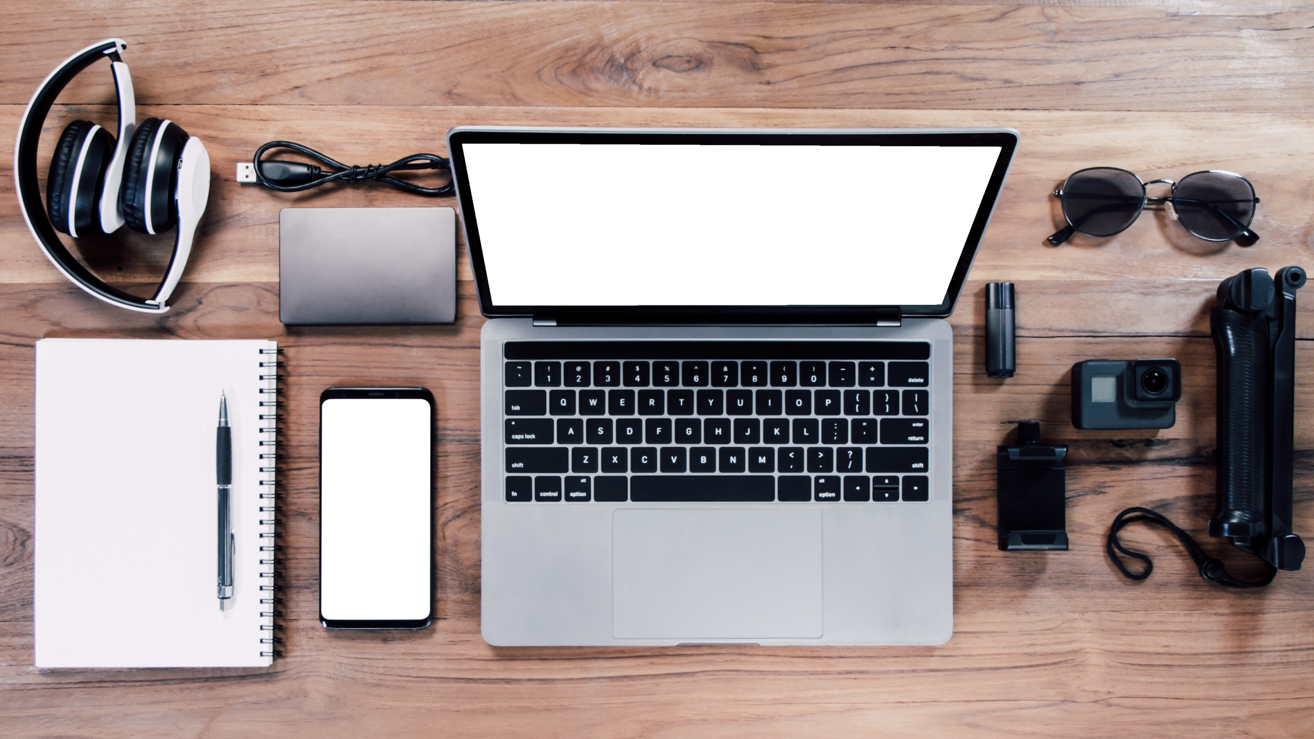 Top view with a digital camera, charger, camera, lens, video camera, USB, personal mockup laptop, book, pen, glasses, headphones, and electronics camera
